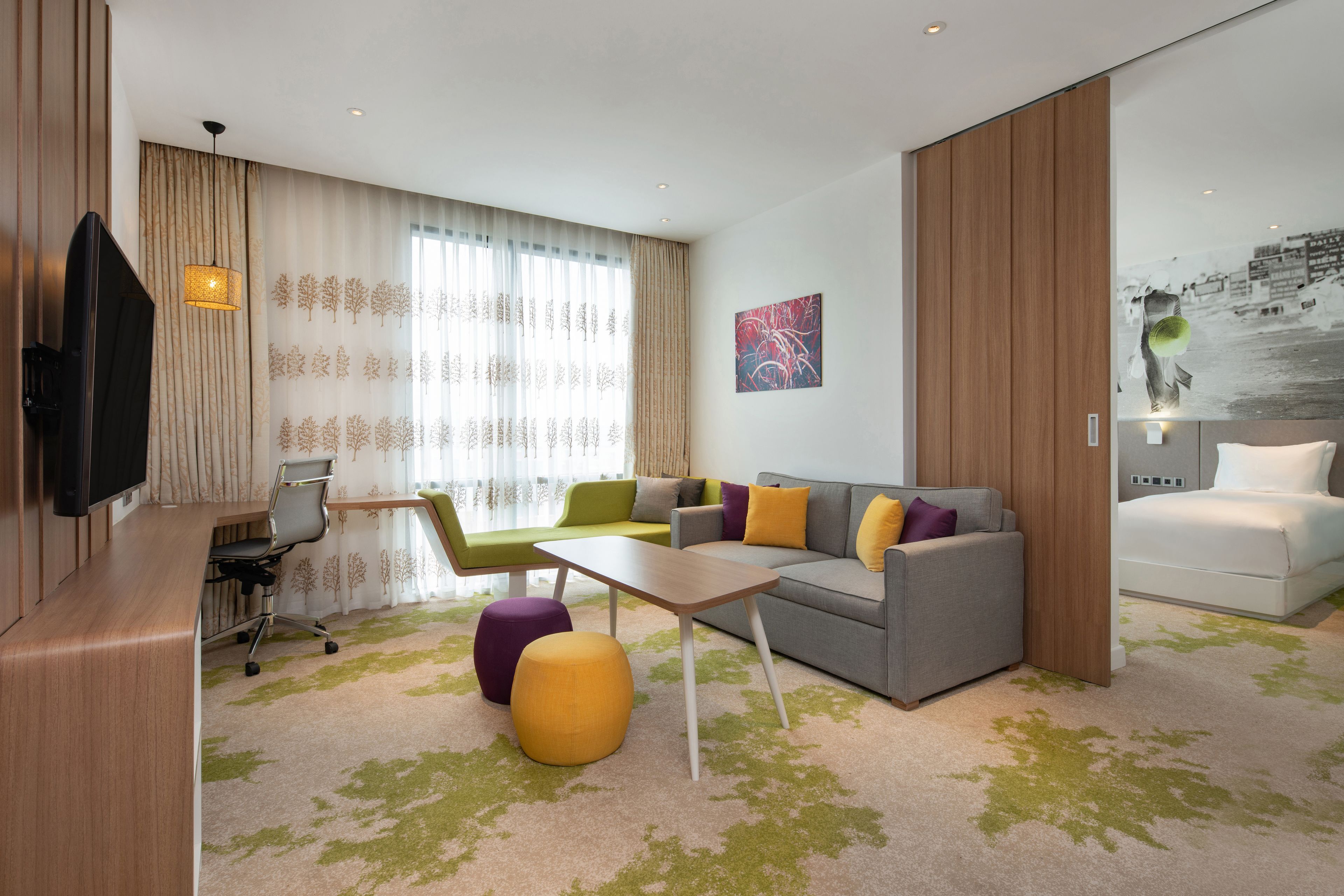 Quarto de hotel moderno com sofá, cadeiras, uma mesinha e televisão.