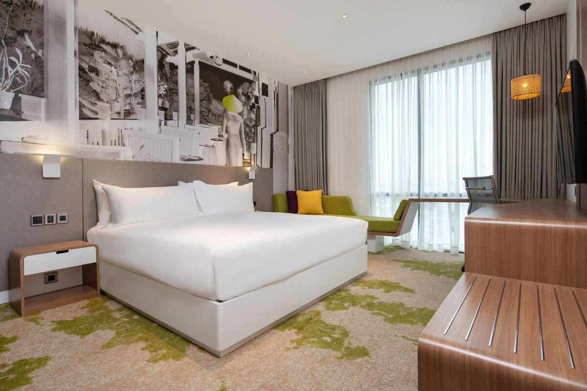 Une chambre d’hôtel moderne avec un grand lit, un bureau, une chaise et une grande fenêtre avec des rideaux.