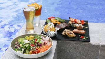 A dining table with a salad, grilled meats, and skewers, along with two glasses of beer.