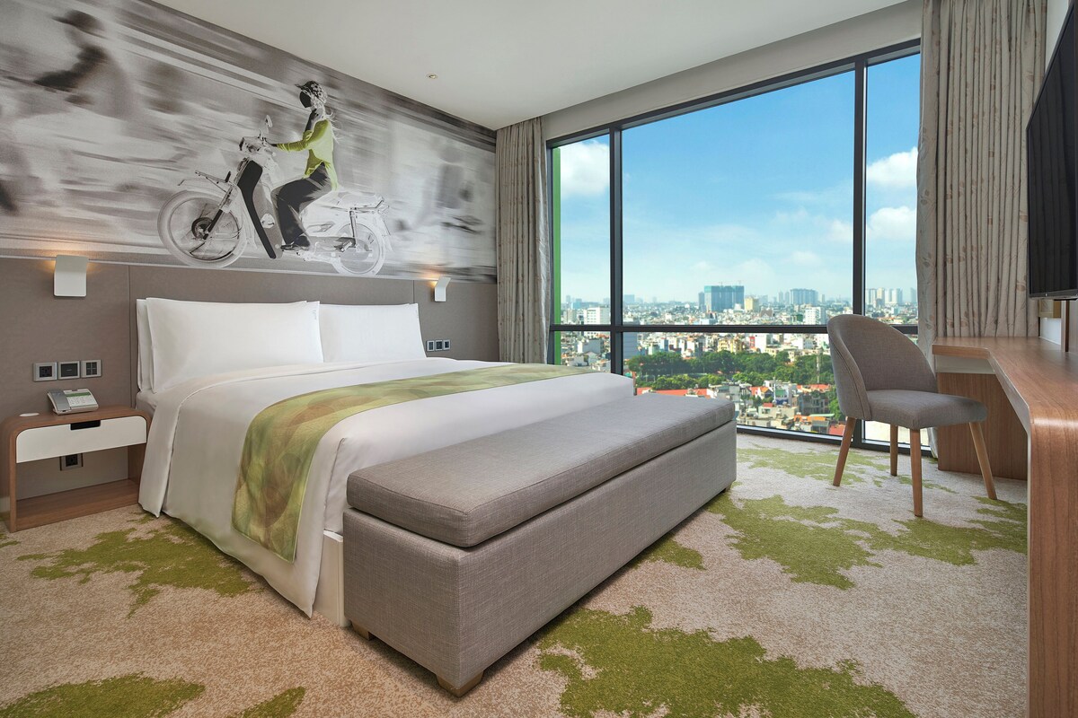 Een moderne hotelkamer met een groot bed, een zithoek met een stoel, een bureau en uitzicht op de stad.