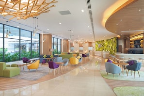 Een moderne hotellobby met diverse zithoeken, een bar en grote ramen met uitzicht op de omgeving.
