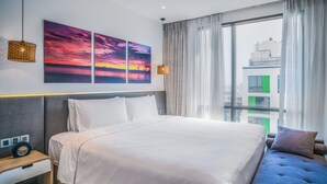Een moderne hotelkamer met een groot bed, een sofa, uitzicht op de stad en kunst aan de muur.