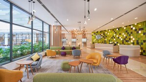 Een moderne hotelentree met grote ramen, kleurrijke zitplaatsen en een groene mozaïekwand.