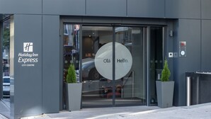 Der Eingang zum Holiday Inn Express City Centre mit einer Glastür, einer digitalen Uhr und zwei Zimmerpflanzen.