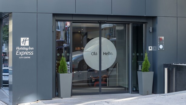 The entrance to Holiday Inn Express City Centre with a glass door, a digital clock, and two potted plants. - Holiday Inn Express Porto City Center by IHG (Porto)