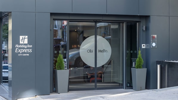 The entrance to Holiday Inn Express City Centre with a glass door, a digital clock, and two potted plants. - Holiday Inn Express Porto City Center by IHG (Porto)