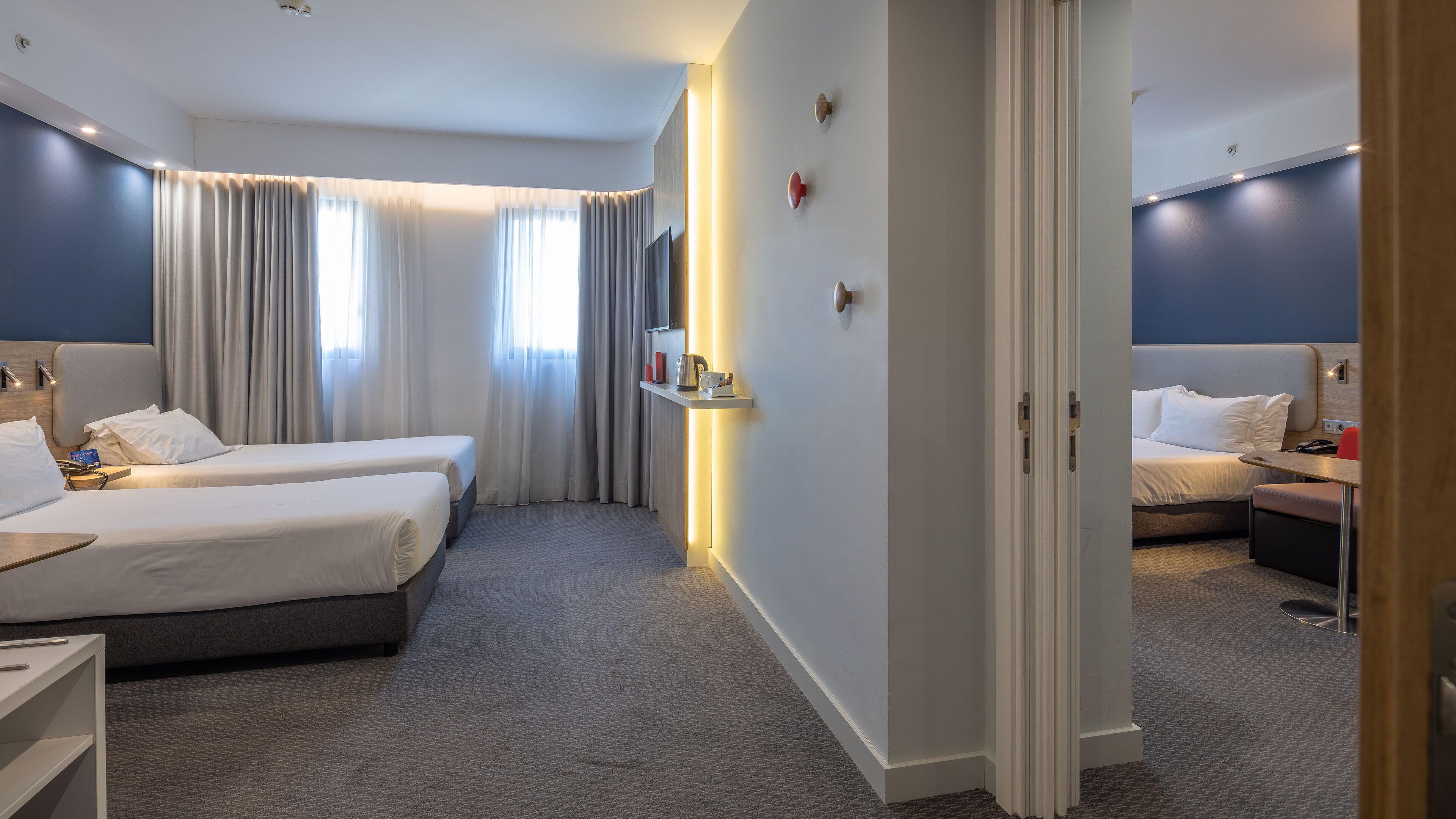 A hotel room with two beds, a desk, a chair, a TV, and a bathroom visible through an open door.