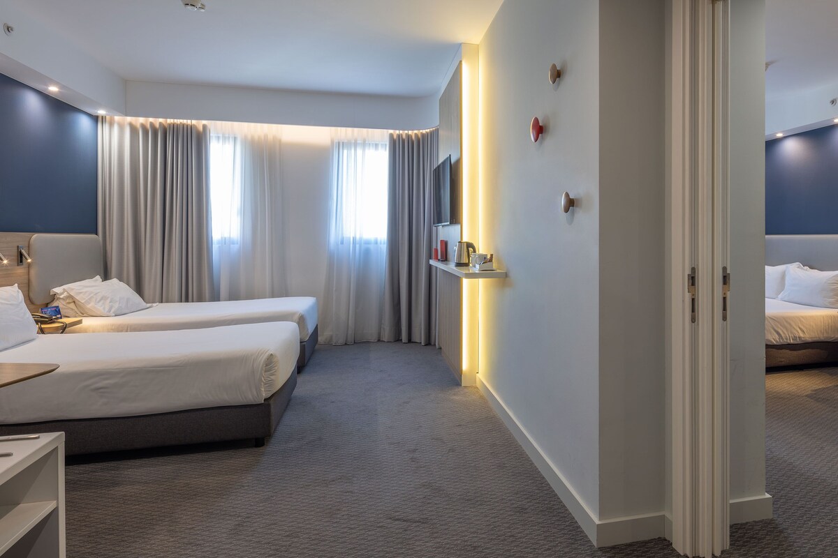 Une chambre d’hôtel avec deux lits, un bureau, une chaise, une télévision et une salle de bain visible à travers une porte ouverte.