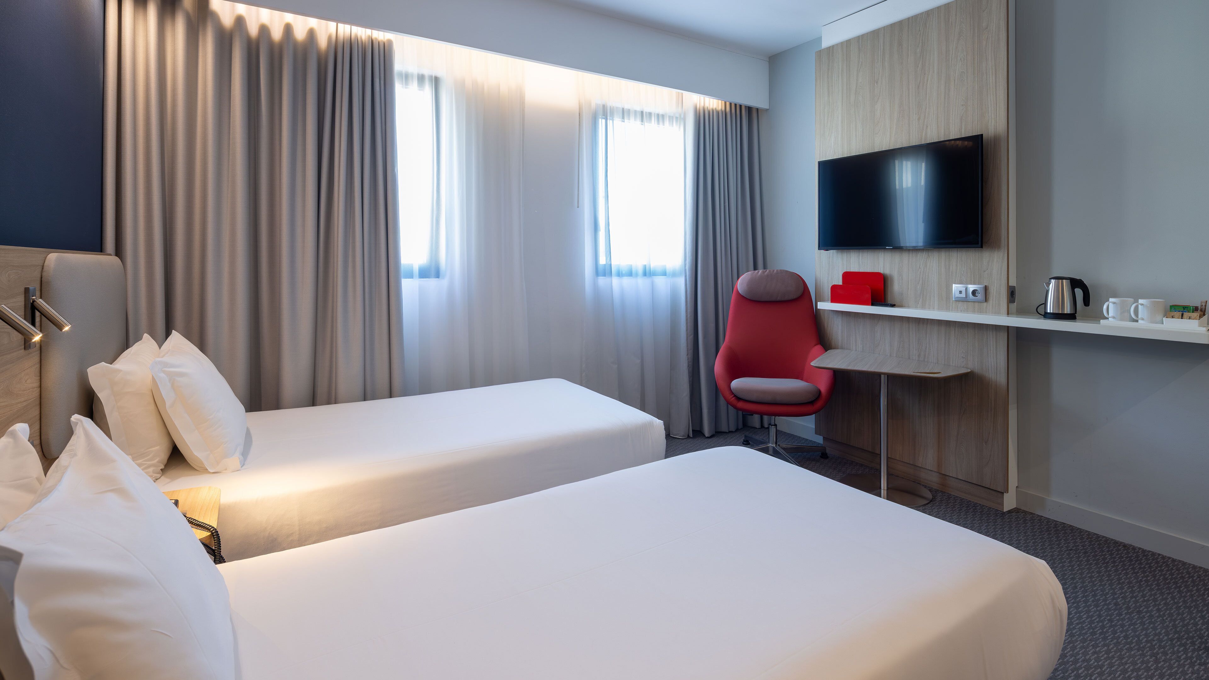 Een hotelkamer met twee bedden, een bureau, een televisie en een rode stoel.