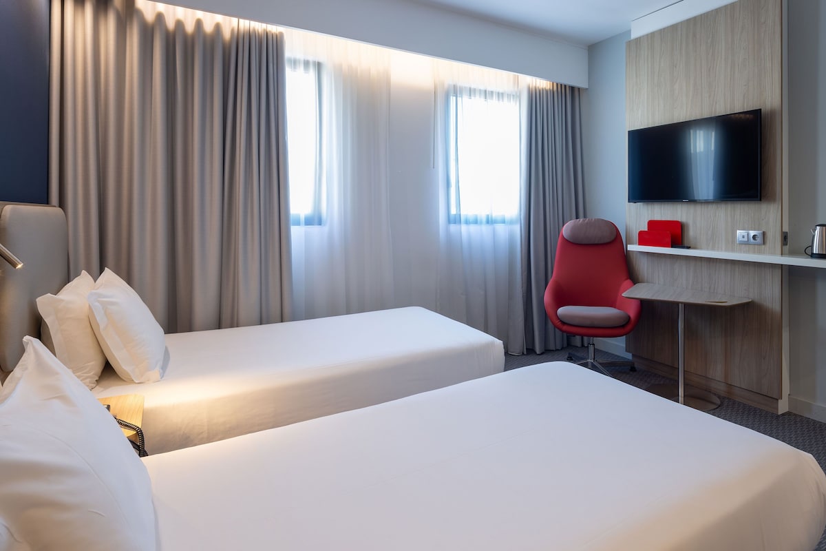 Une chambre d’hôtel avec deux lits, un bureau, une télévision et une chaise rouge.