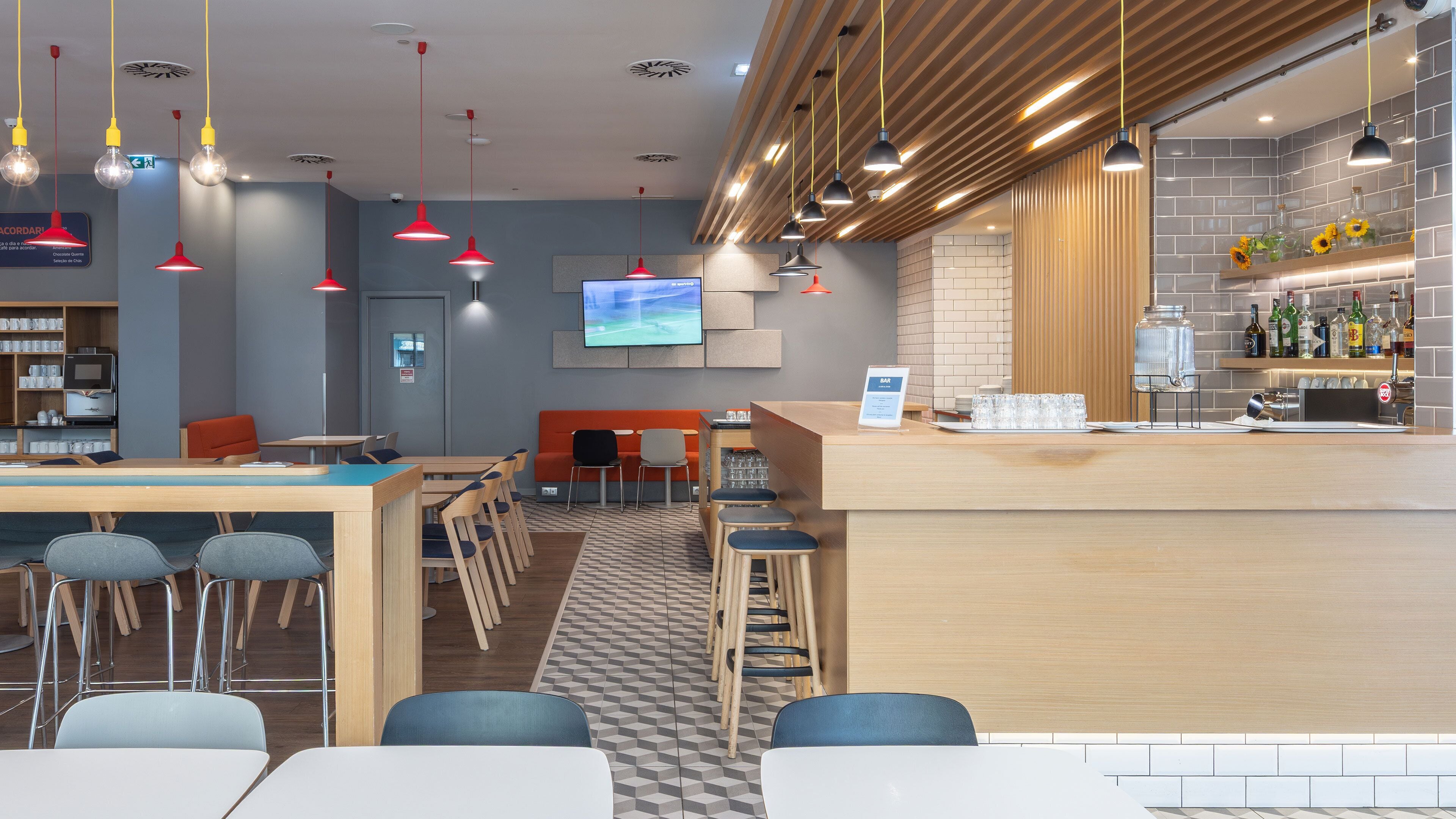 Un café moderno con zona de bar, mesas y sillas, y una pantalla de televisión.