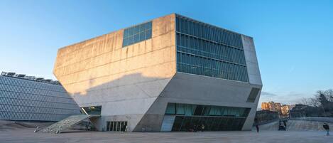 A modern building with a unique angular design, large windows, and a spacious plaza in front.