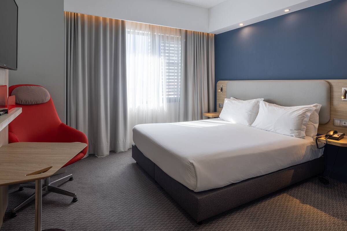 Hotellihuone, jossa on sänky, työpöytä, tuoli ja televisio.