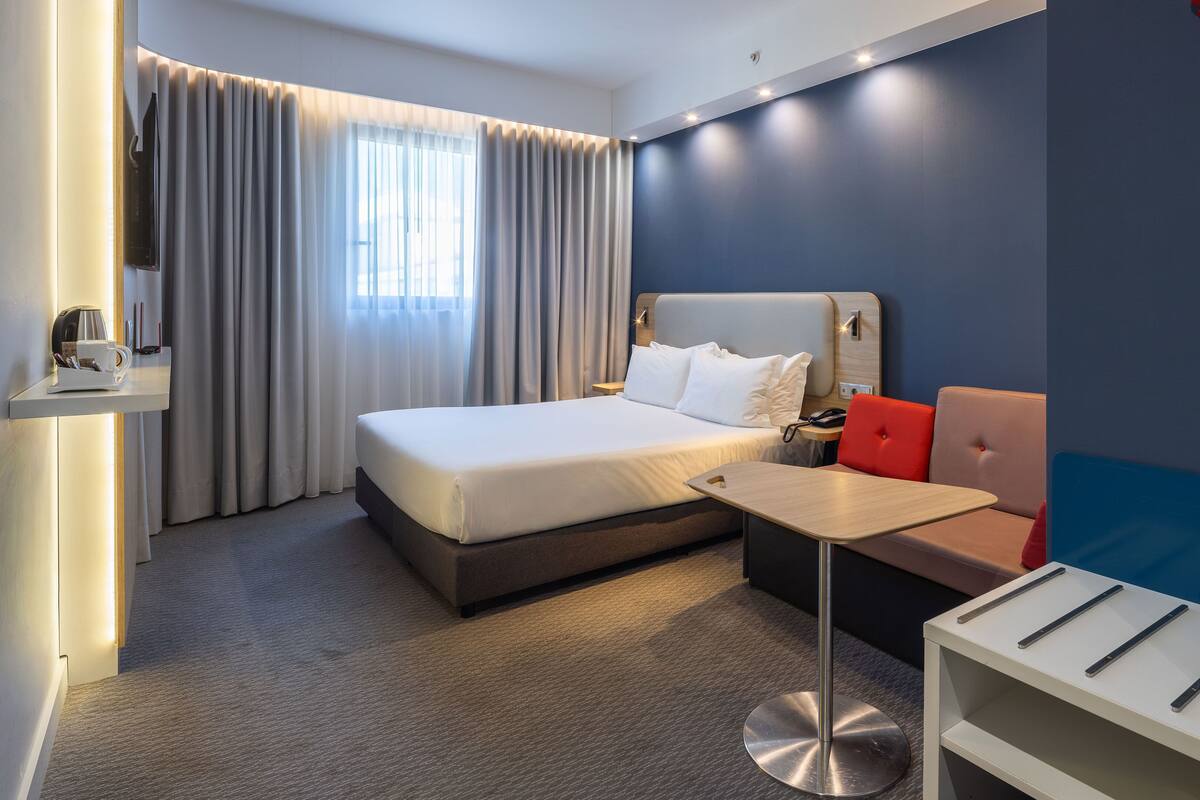 Moderni hotellihuone, jossa on suuri sänky, työpöytä ja sohva.