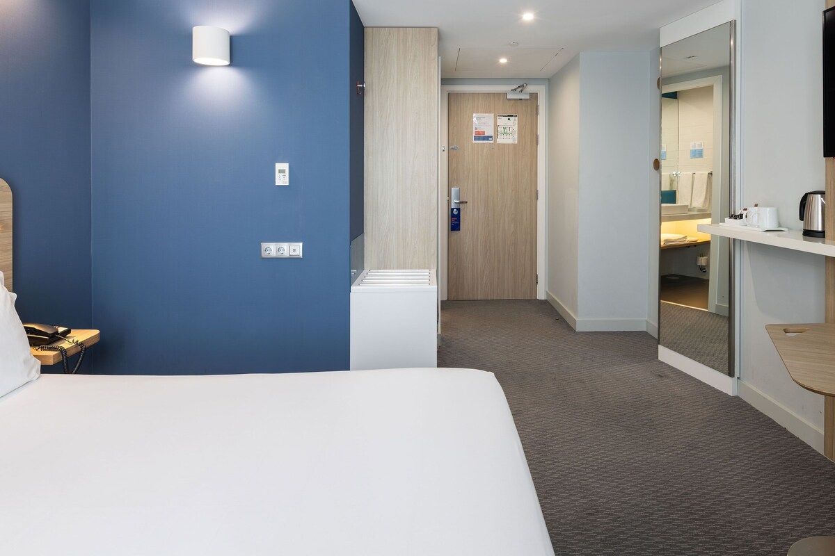 Une chambre d’hôtel avec un lit, un bureau, un miroir et une télévision.