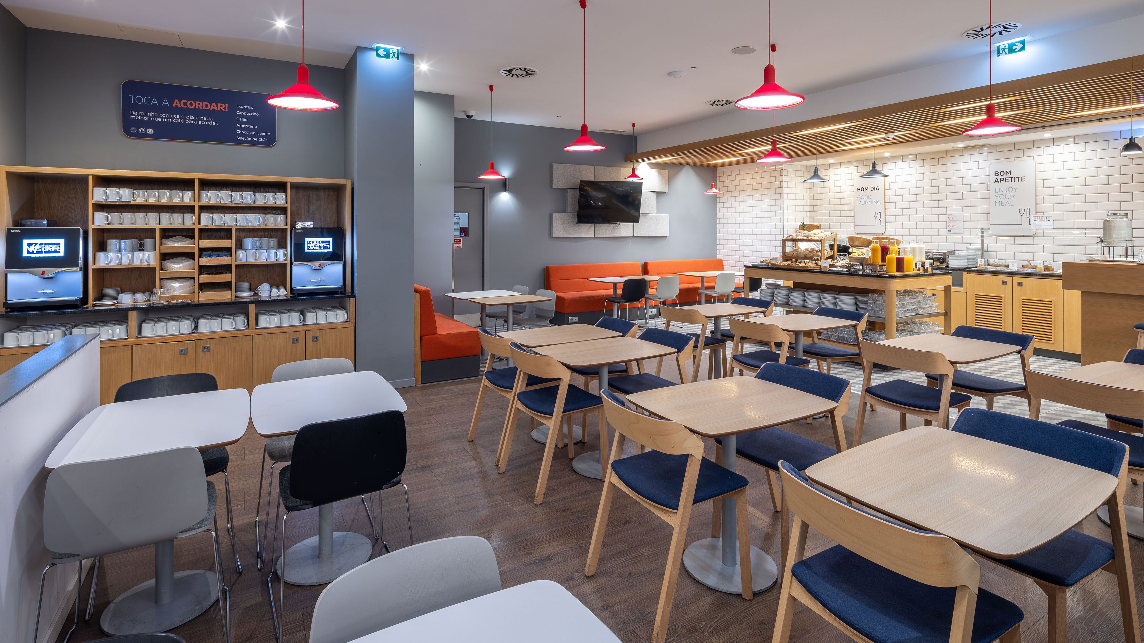 Un café moderne avec des tables et des chaises en bois, un comptoir où sont exposés des plats et des boissons, et un tableau affichant le menu au-dessus du comptoir.