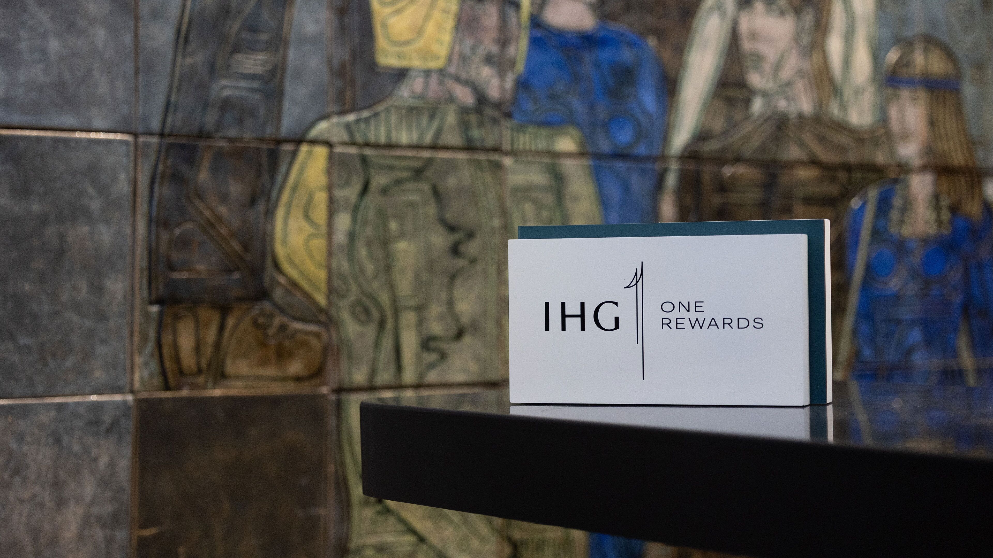 Un letrero con 'IHG ONE REWARDS' en una superficie reflectante, posiblemente un área de recepción, con un fondo de vitral.