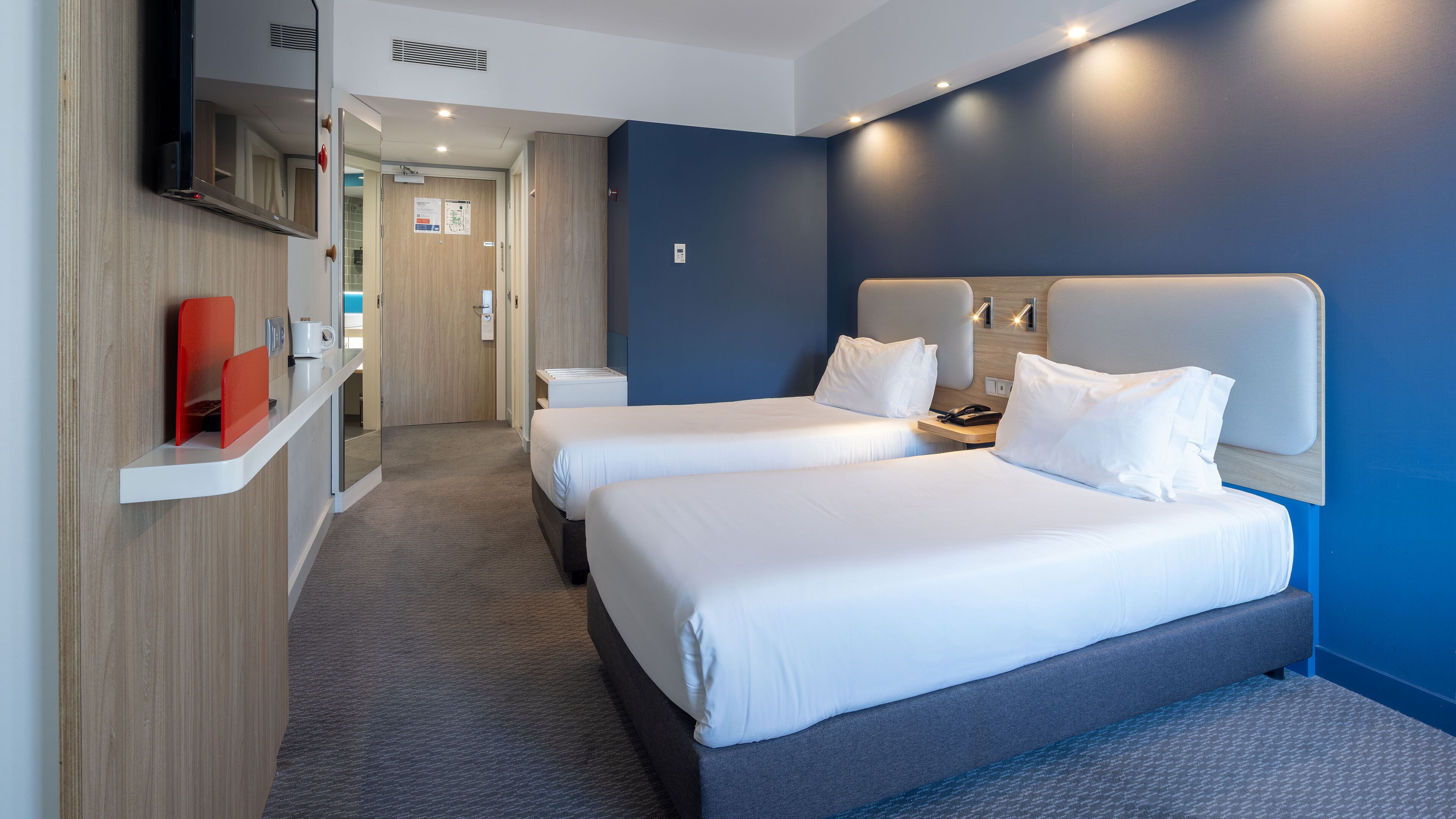 A hotel room with two beds, a desk, a TV, and a bathroom.