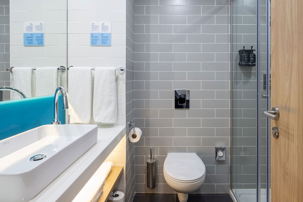 Une salle de bain moderne avec un lavabo blanc, un receveur de douche bleu et une paroi de douche en verre.