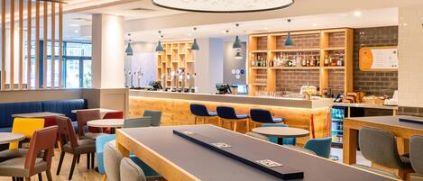 A modern cafe with wooden tables and chairs, a bar area, and shelves stocked with beverages.