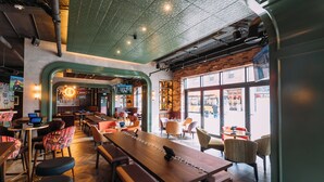 A modern restaurant with a long wooden table, cushioned chairs, and a brick wall.