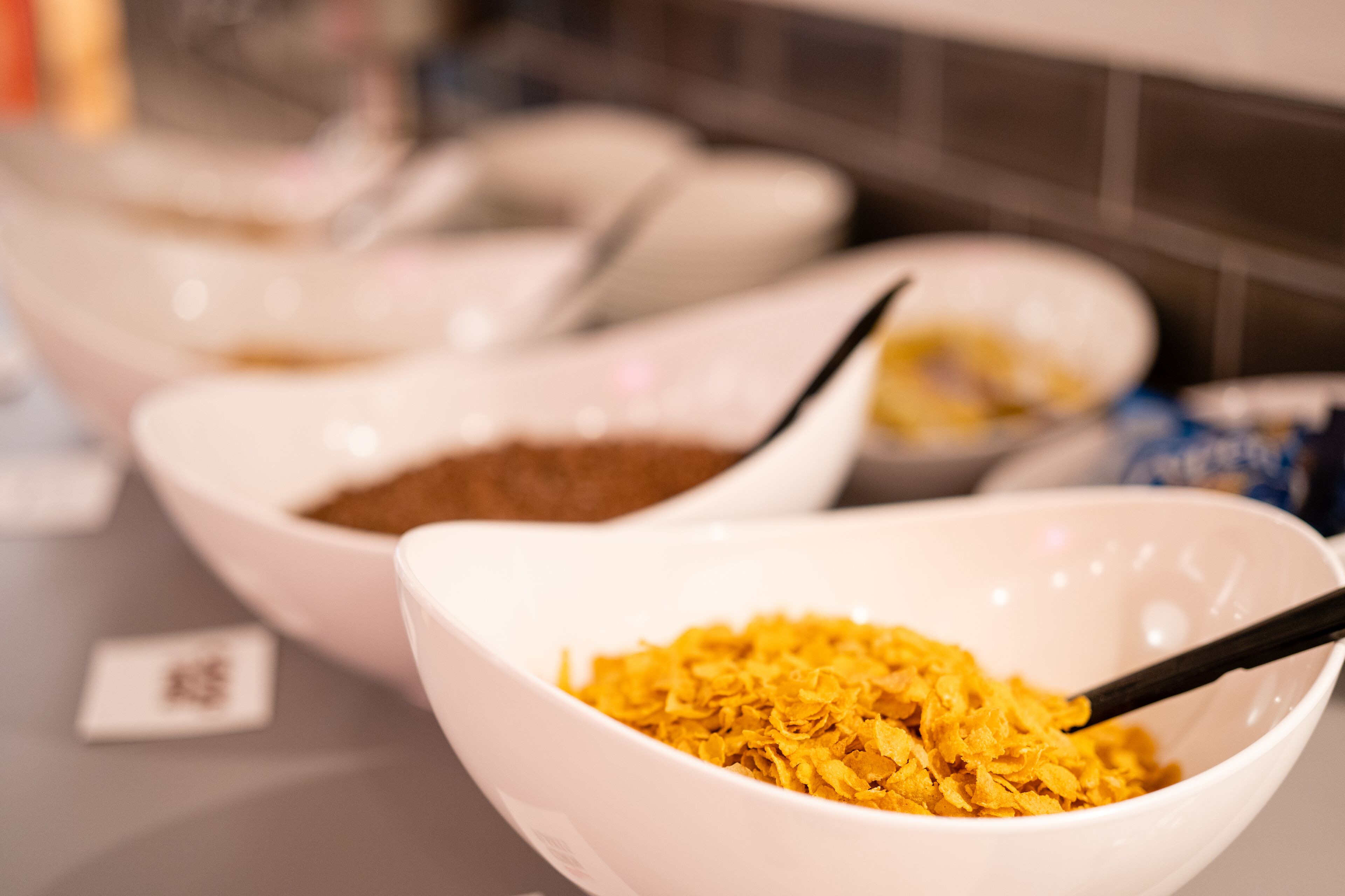 A close-up of a bowl with a spoon, containing a yellowish substance, possibly cereal flakes, on a table.