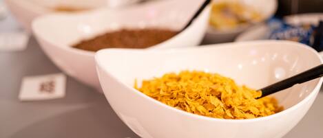 A close-up of a bowl with a spoon, containing a yellowish substance, possibly cereal flakes, on a table.