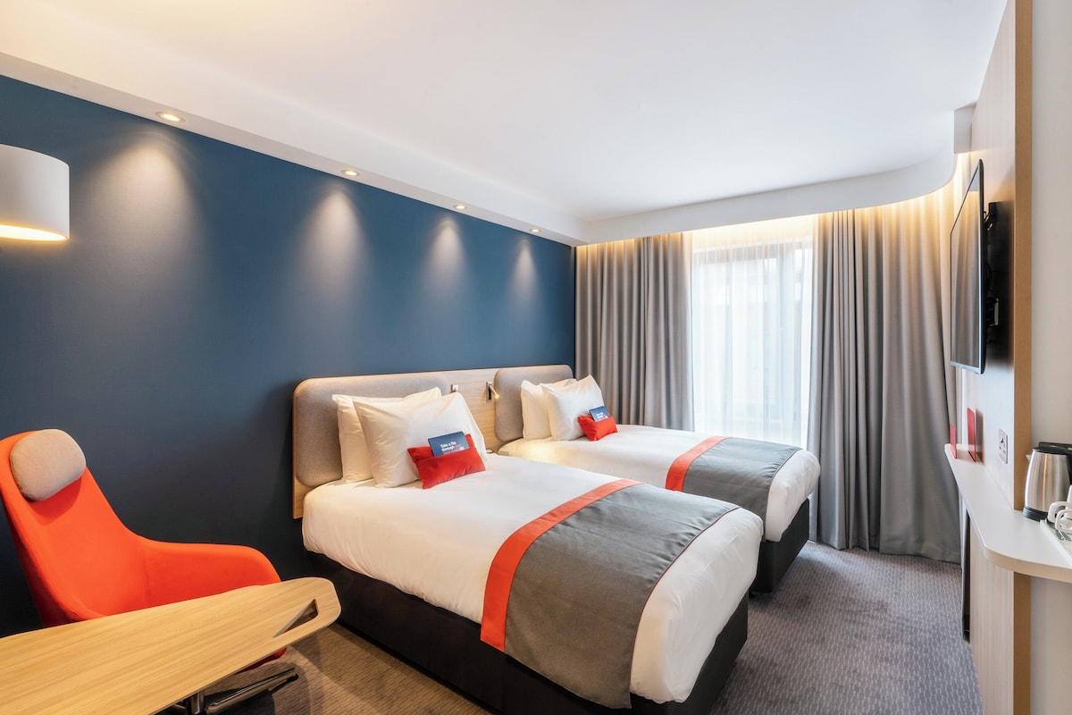 A hotel room with two beds, a desk, and a TV.