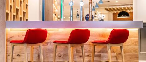 A bar area with wooden paneling, three red bar stools, and a counter with multiple taps.
