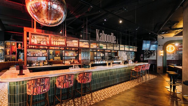 A bar area with a counter, stools, shelves with bottles, and a disco ball.