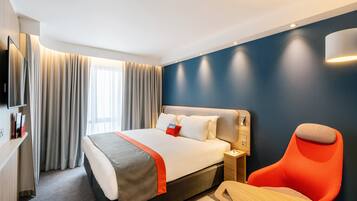 Een hotelkamer met een bed, een bureau, een stoel, een televisie en gordijnen.