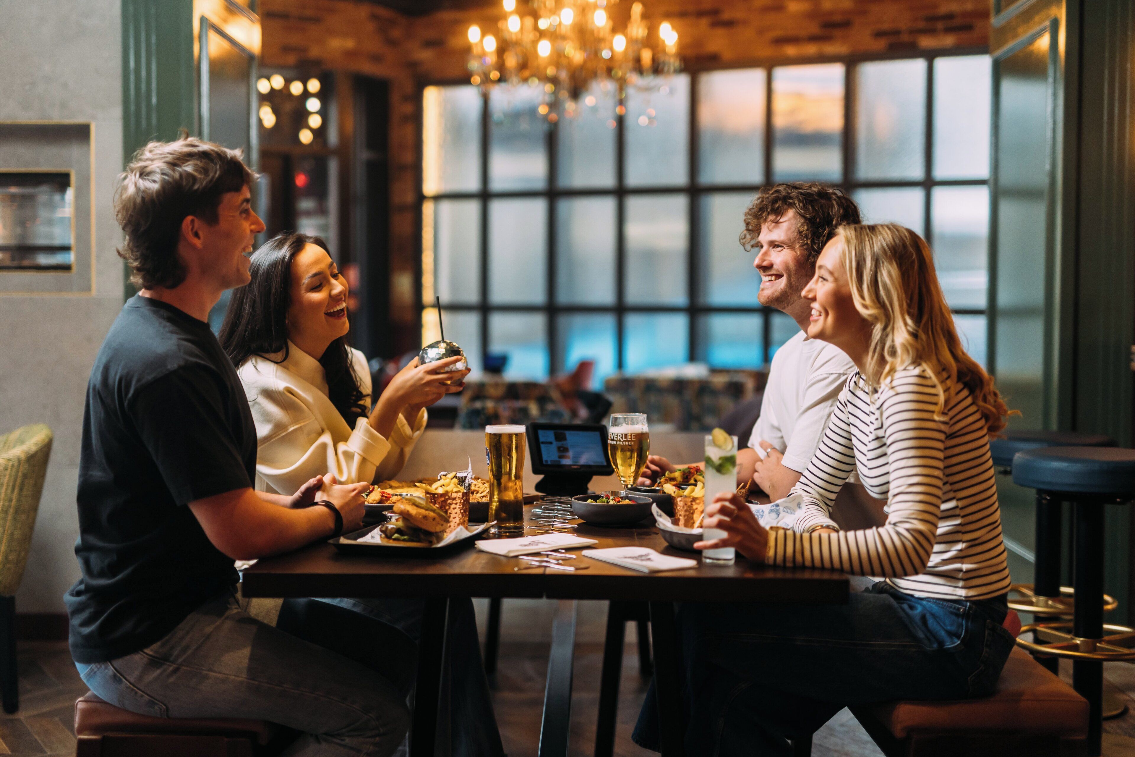 Un grupo de personas cenando en un restaurante con un amplio ventanal y un candelabro.