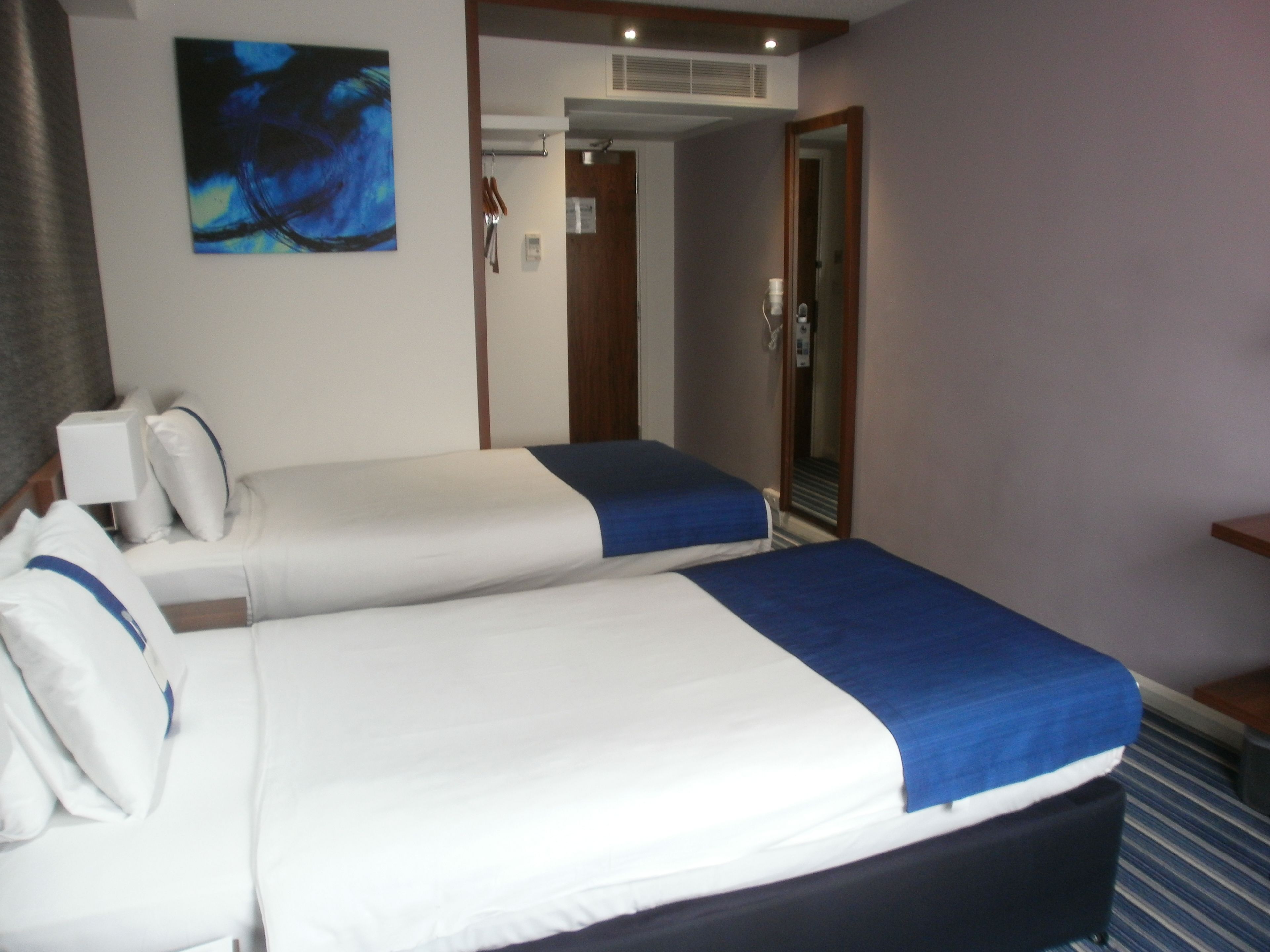 A hotel room with two beds, a painting on the wall, and a door leading to another room.