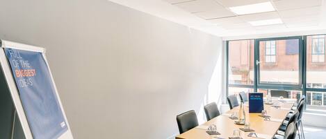 A conference room with a long table, chairs, a whiteboard, and a window with a view of buildings.