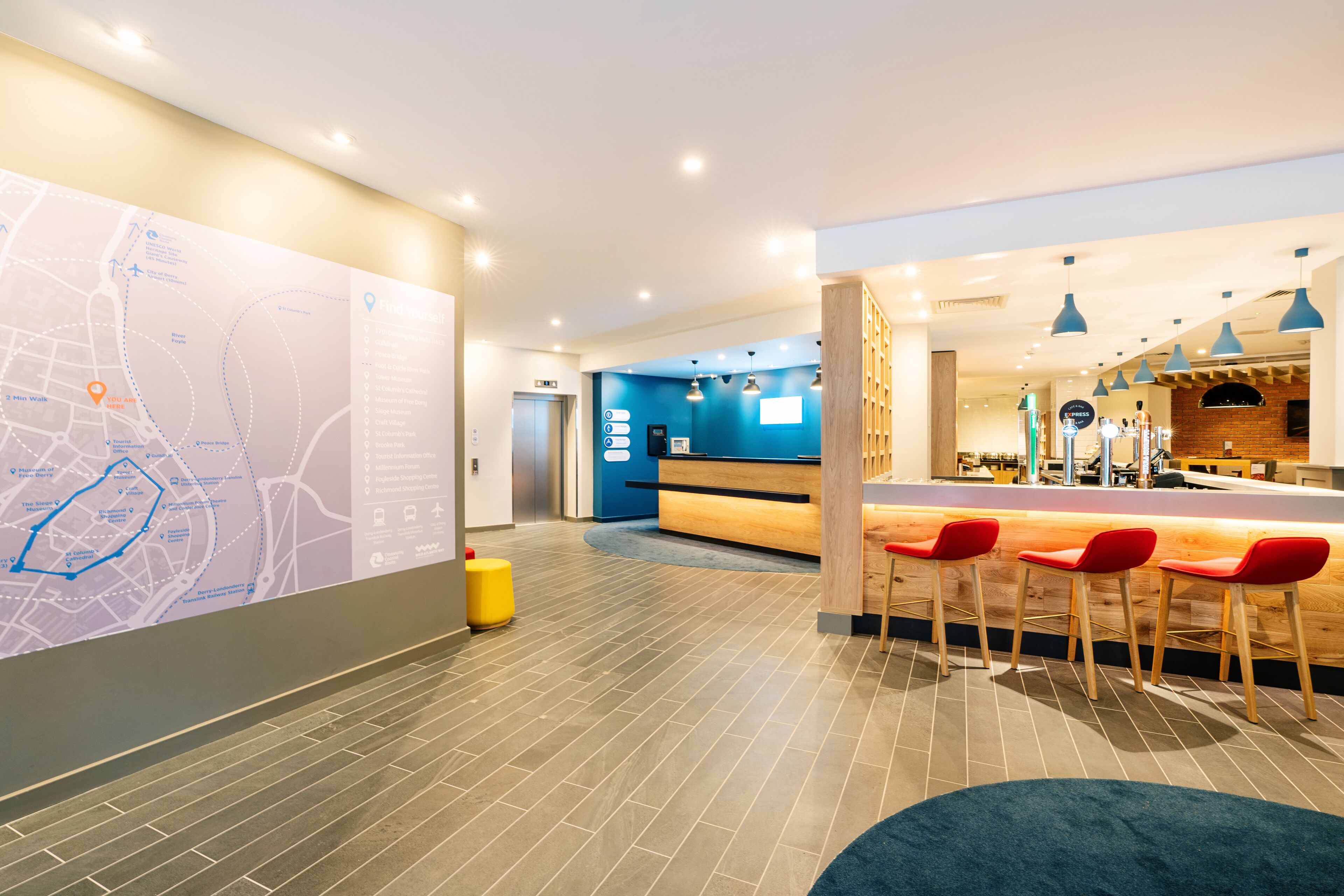 A hotel lobby with a large map on the wall, a reception desk, and a bar area with red chairs.