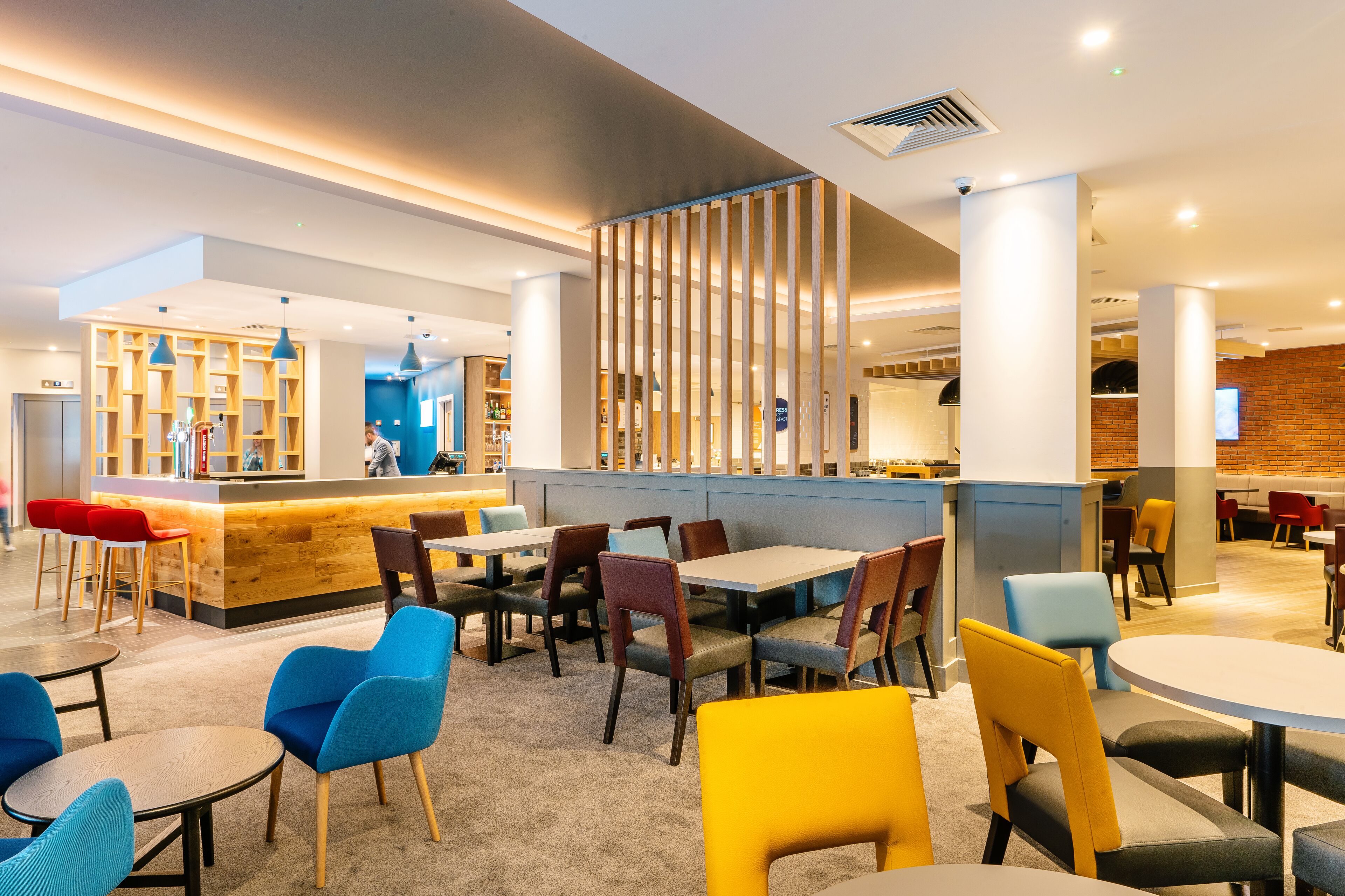 Un restaurante moderno con una zona de bar, múltiples opciones de asientos, incluyendo mesas redondas y sillas, y una cocina visible al fondo.