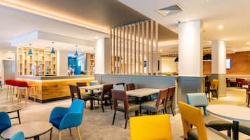 Un restaurante moderno con una zona de bar, múltiples opciones de asientos, incluyendo mesas redondas y sillas, y una cocina visible al fondo.
