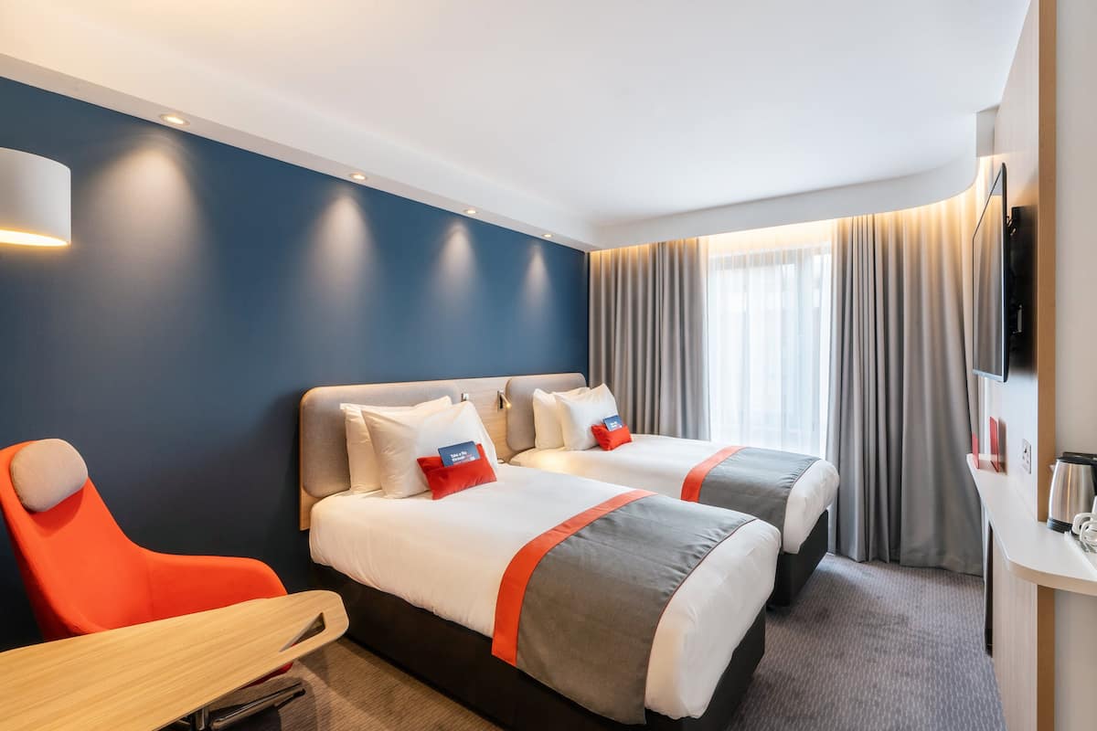 Habitación de hotel con dos camas, un escritorio y un televisor.