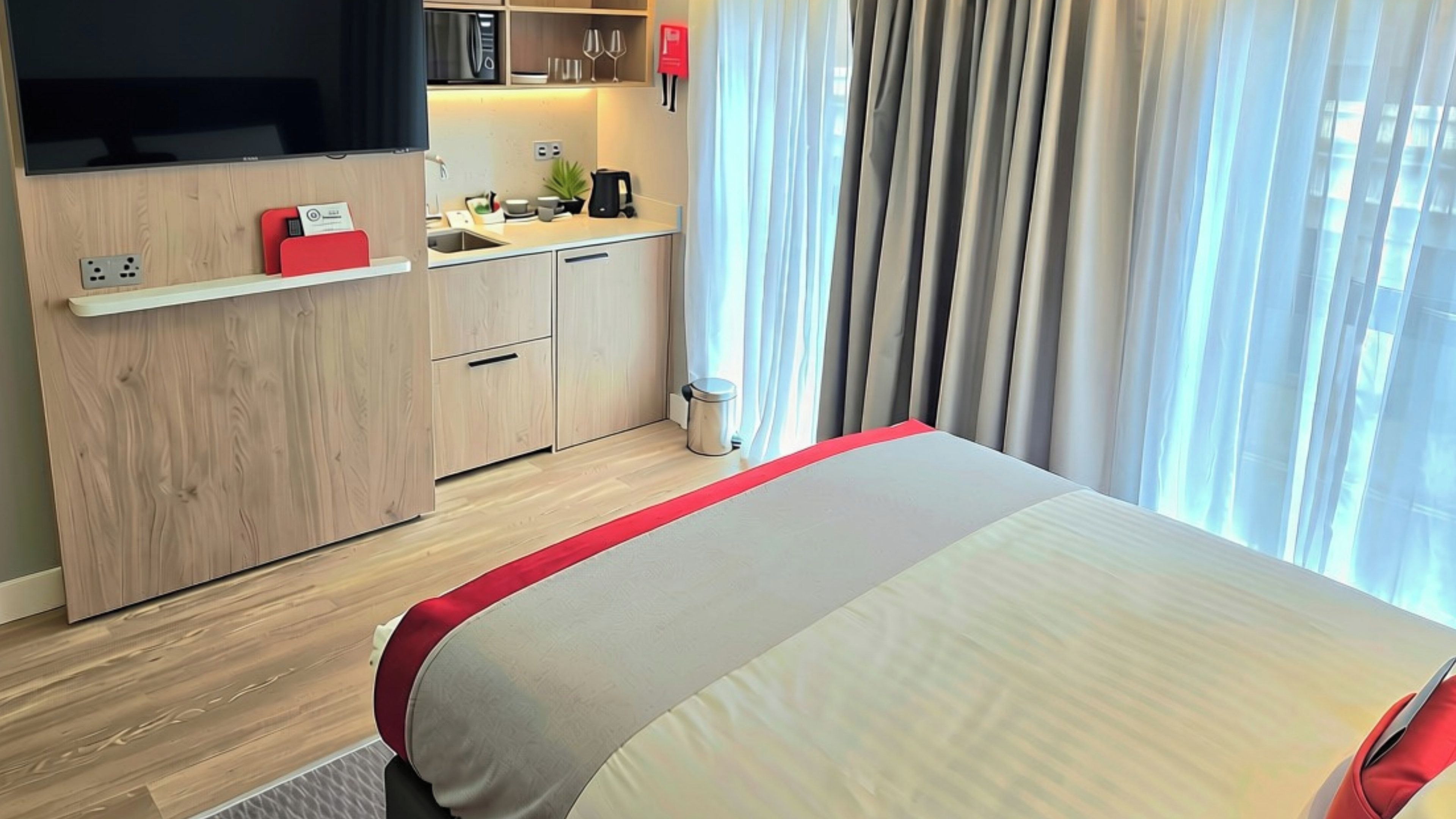 Une chambre d’hôtel avec un lit, une kitchenette, une télévision et une fenêtre avec des rideaux.