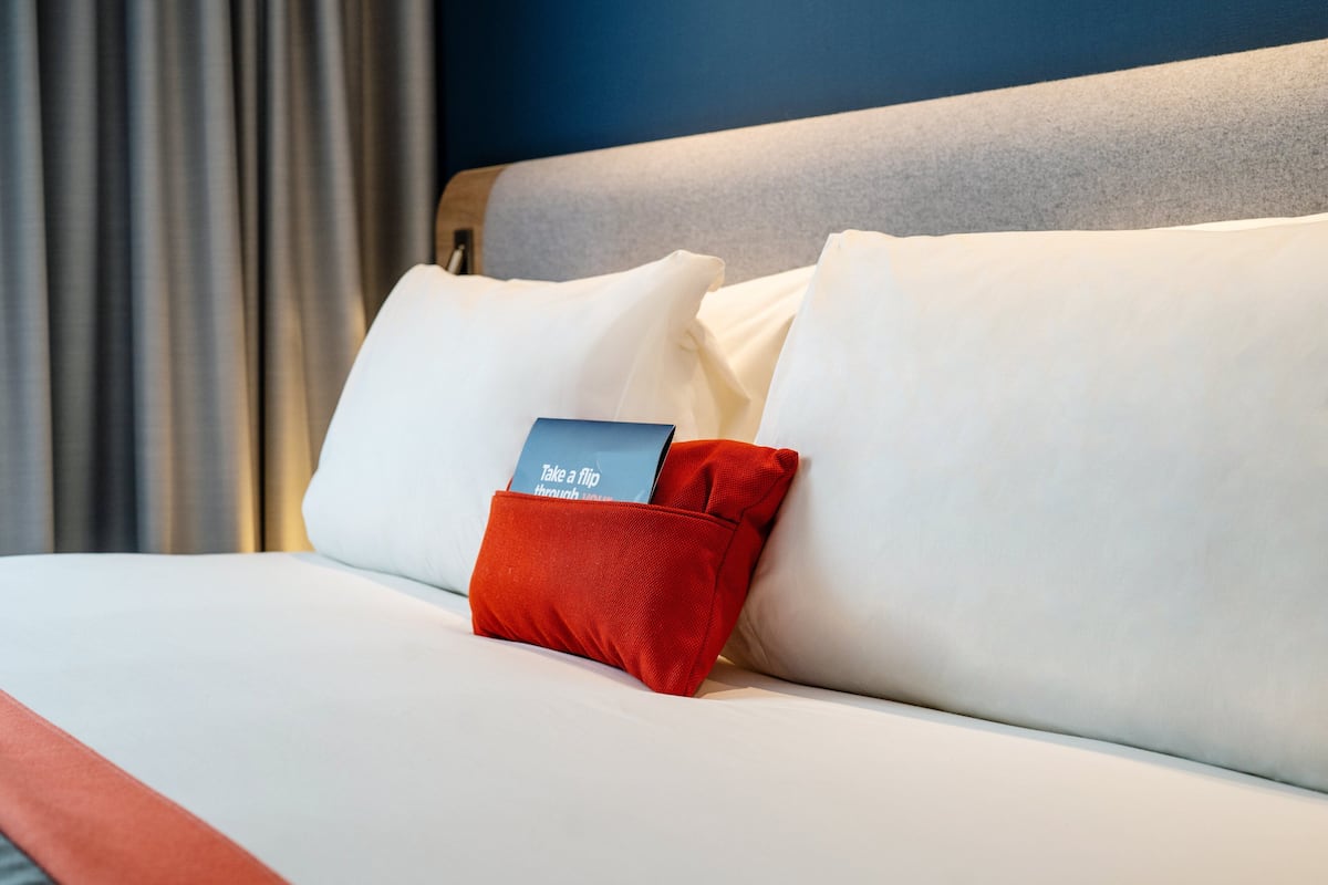 Una cama bien hecha con ropa de cama blanca y una almohada roja con una etiqueta.