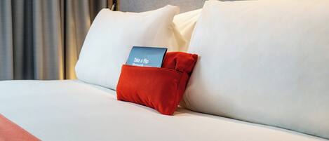 A neatly made bed with white bedding and a red pillow with a tag.