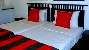 A double bed with white and red bedding, a black headboard, and a white nightstand.