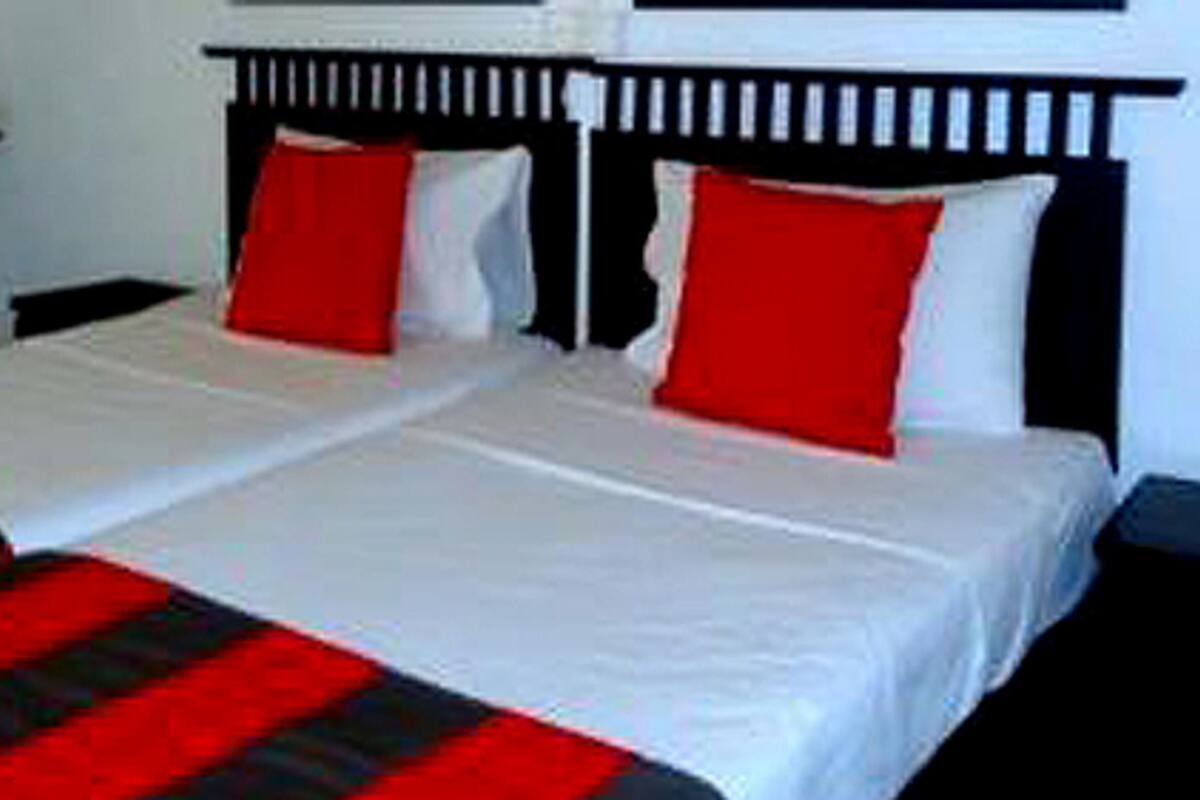 Una cama doble con ropa de cama blanca y roja, un cabecero negro y una mesita de noche blanca.