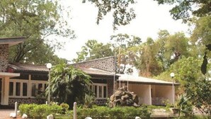 A building with a stone facade, a covered entrance, and a garden with a statue and plants.
