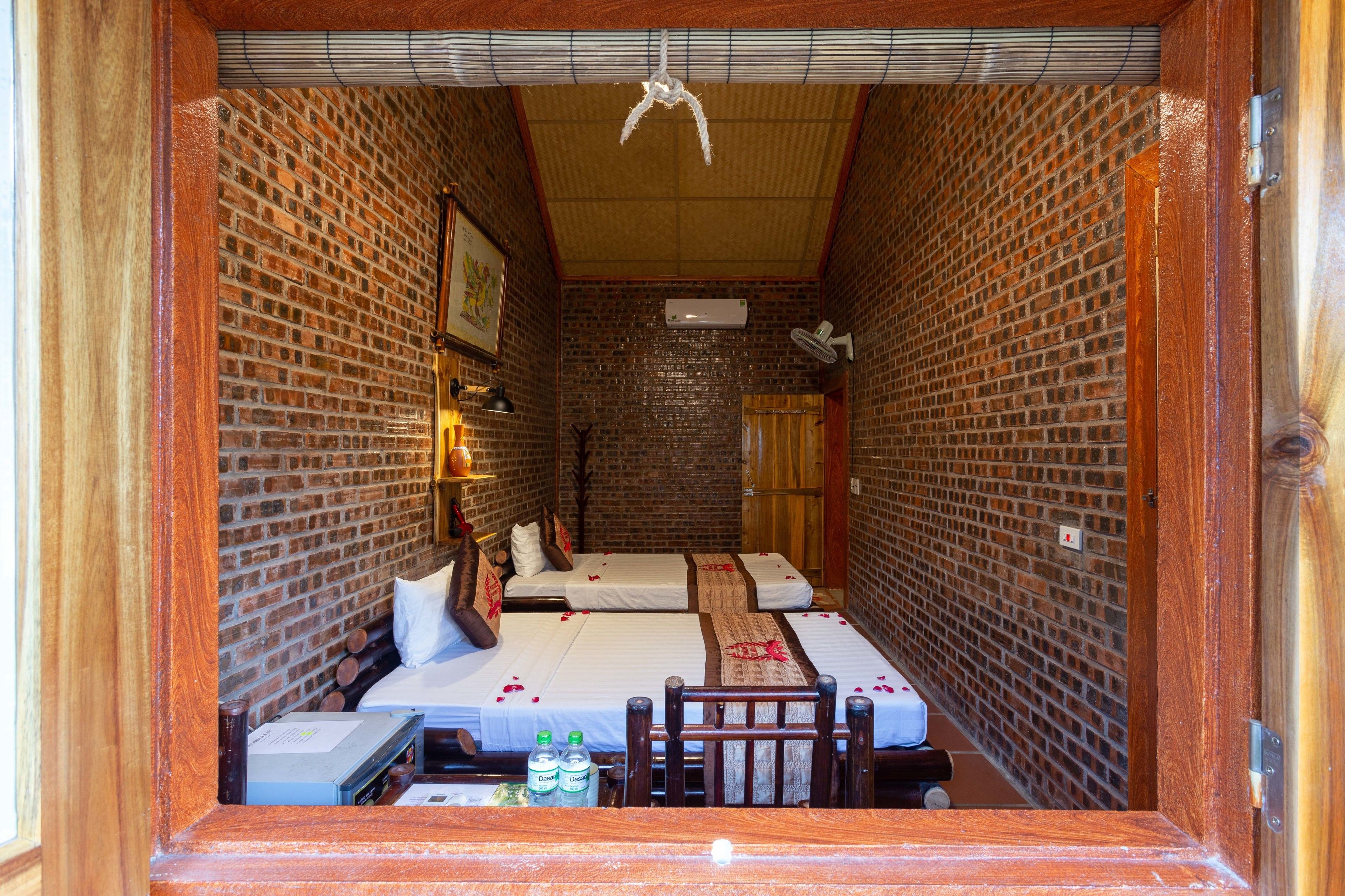Una habitación con paredes de ladrillo, dos camas, una mesa con botellas y una silla.