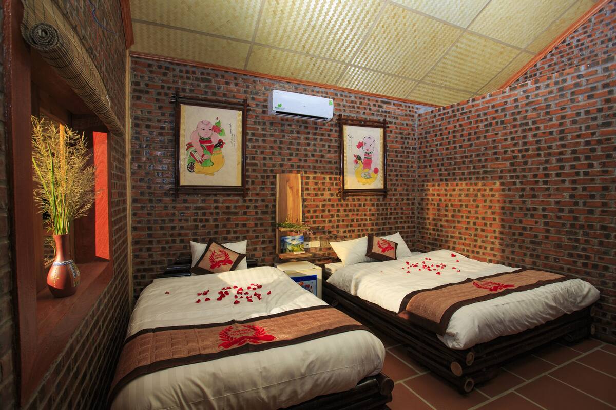 Een hotelkamer met bakstenen muren, twee bedden, een groot raam en een plafondventilator.
