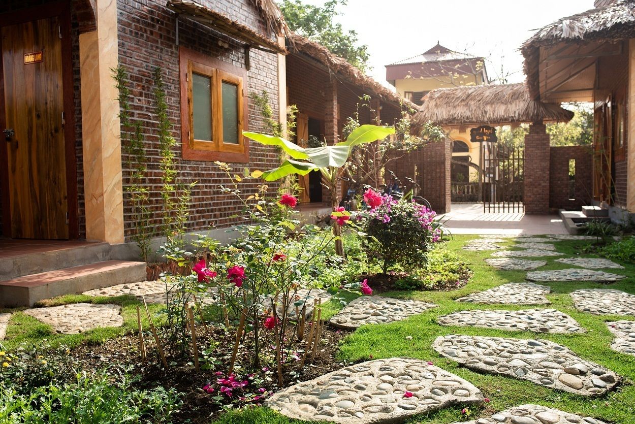 A traditional brick building with a thatched roof, a stone pathway, and a garden with pink flowers.
