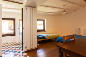 A room with a wooden floor, a bed with a green blanket, a table, and a window with blinds. - La Costa de Mollo (Mollo)