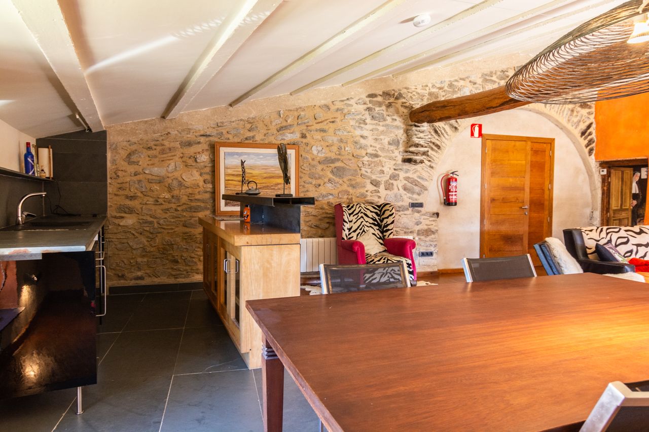 A rustic interior with a stone wall, wooden furniture, and a fireplace.