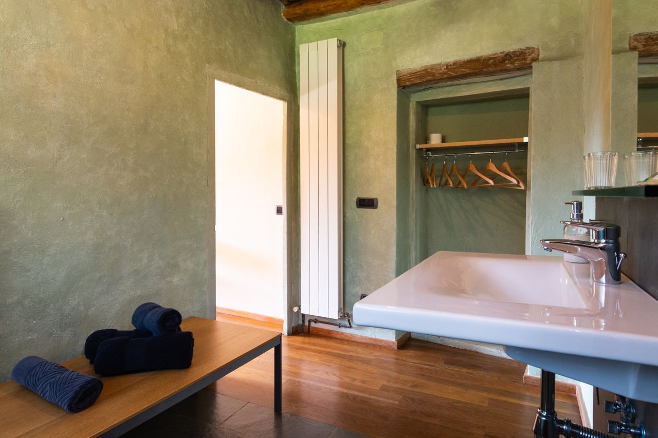A modern bathroom with a large white sink, wooden floor, and a towel rack with hangers.